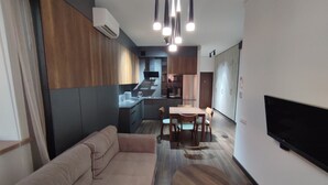 A modern living room with a sofa, a dining table with chairs, a TV mounted on the wall, and a kitchen area in the background. -  A rare minimalist concept in a quiet location with skyline view (Yerevan)
