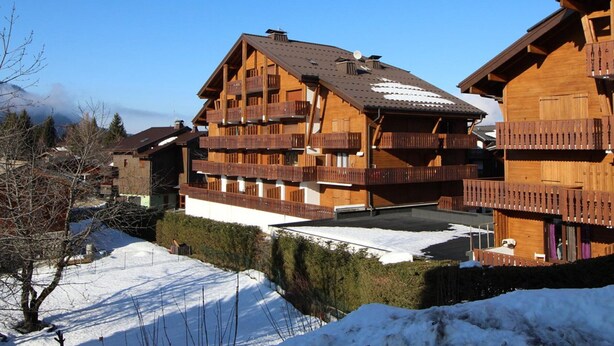 A multi-story wooden chalet with balconies, a ski slope in the background, and a clear blue sky. - Spacious studio 4 pers with garage and dishwasher in Les Carroz (Les Carroz d'Arâches)