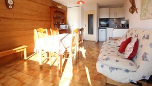 A cozy living room with a wooden dining table and chairs, a sofa with patterned cushions, and a kitchen area with cabinets and appliances. - Spacious studio 4 pers with garage and dishwasher in Les Carroz (Les Carroz d'Arâches)