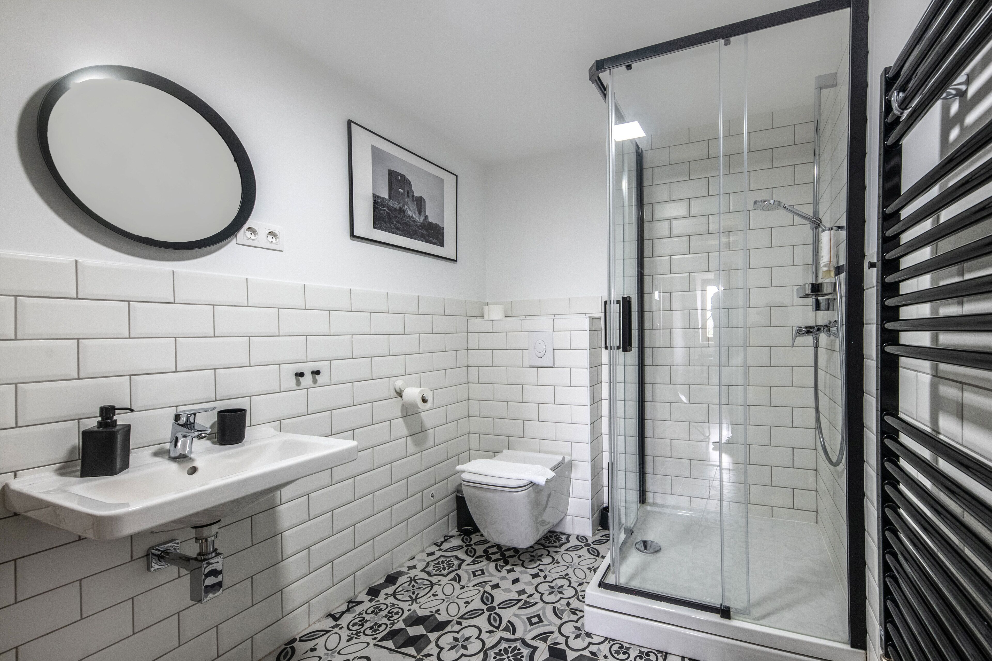 A modern bathroom with a white sink, black soap dispenser, and a glass shower enclosure.