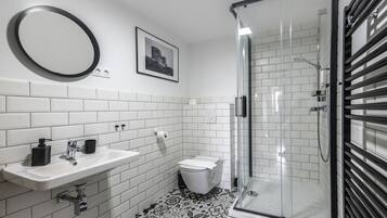 A modern bathroom with a white sink, black soap dispenser, and a glass shower enclosure.