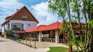A rustic building with a stone facade and a red roof, featuring outdoor seating and a large wooden wheel. - Ferrata Guesthouse (Csesznek)
