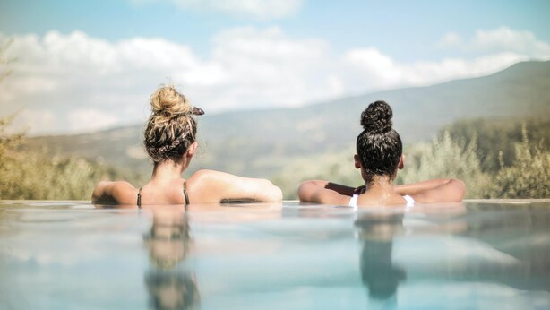 Two people sitting in a hot tub with a mountainous landscape in the background. - Ferrata Guesthouse (Csesznek)