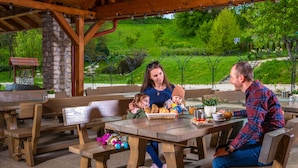 A wooden picnic table with benches, surrounded by a stone wall and a wooden pergola. - Ferrata Guesthouse (Csesznek)
