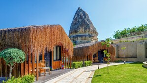 Een resort met gebouwen met rieten daken, een verharde looppad en een opvallende rotsformatie op de achtergrond.
