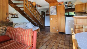 Un salon chaleureux avec un escalier en bois, un canapé à rayures rouges et un sol carrelé.