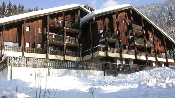 Un immeuble en bois à plusieurs étages, doté de balcons, et entouré de neige.
