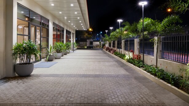 A paved walkway with potted plants and a building with large windows and a red awning. - 7 Apple Hotel Nashik (Nashik)