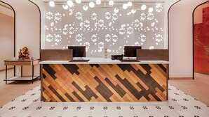 A reception desk with a geometric patterned wall, two black monitors, and a decorative statue on a side table. - 7 Apple Hotel Nashik (Nashik)