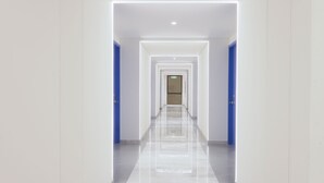 A modern, well-lit hallway with a reflective floor, leading to a door at the end. - 7 Apple Hotel Nashik (Nashik)
