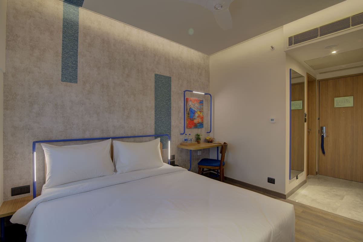A hotel room with a bed, a desk, a chair, and a mirror.