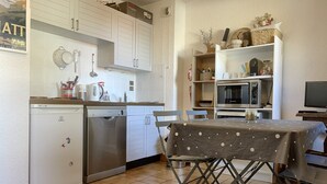 Una cocina compacta con armarios blancos, lavavajillas, microondas y una mesa de comedor con mantel estampado de lunares.