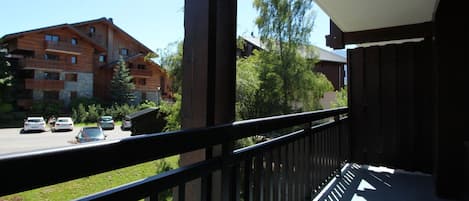 A balcony with a view of a multi-story building, a road with cars, and greenery.