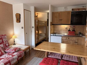 Ein gemütlicher Raum mit Etagenbett, einer Küchenzeile, einem Esstisch und einer Couch mit herzförmigen Kissen.
