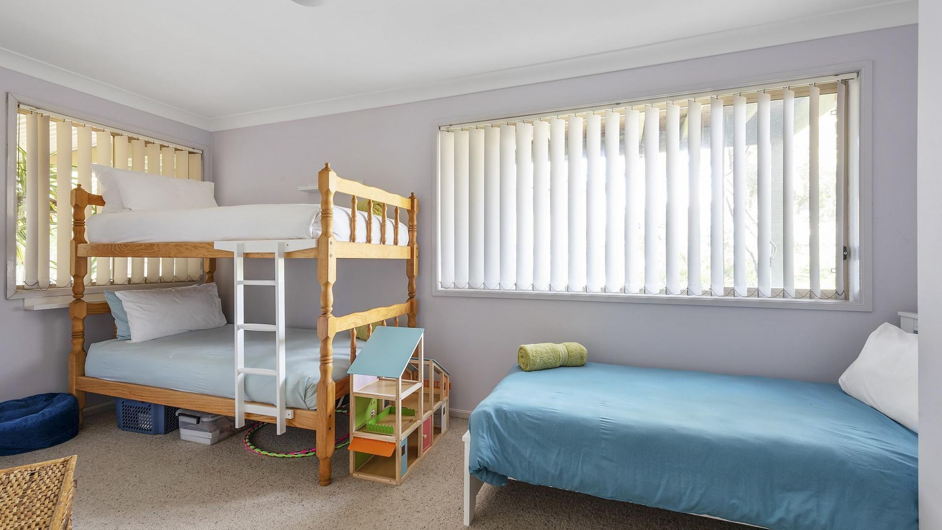A bunk bed room with a single bed, a play area, and large windows with blinds.