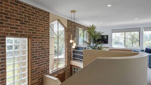 Un interior moderno con paredes de ladrillo visto, una escalera curva y ventanas amplias que ofrecen vistas a la vegetación.