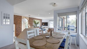 Un comedor con una mesa de madera, sillas blancas y protectores de mesa tejidos.