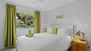 Un dormitorio con cama, mesita de noche, lámpara, un cuadro y cortinas verdes.