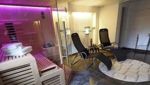 A modern spa room with a sauna, massage chairs, and a small table with a candle.