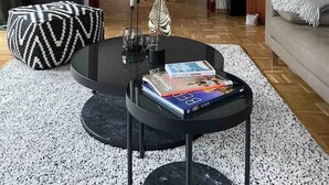 A modern living room with a round coffee table, a sofa, a dining area in the background, and a large window.