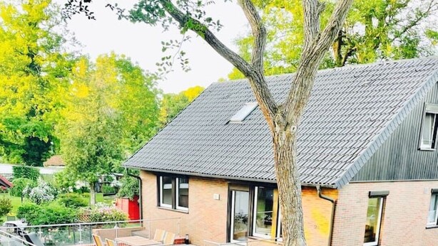A modern house with a sloped roof, a covered patio, and a well-maintained garden.