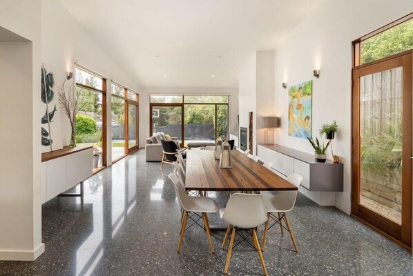A modern kitchen with a long dining table, white chairs, and a view through large windows. - Sorrento Sea Escape. (Sorrento)