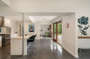 Une cuisine moderne dotée d’un îlot central, d’un coin repas avec des chaises et d’une grande fenêtre qui laisse entrer la lumière naturelle.