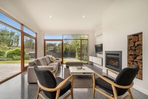 Un salon moderne avec un canapé, des fauteuils, une table basse, une cheminée et de grandes fenêtres.