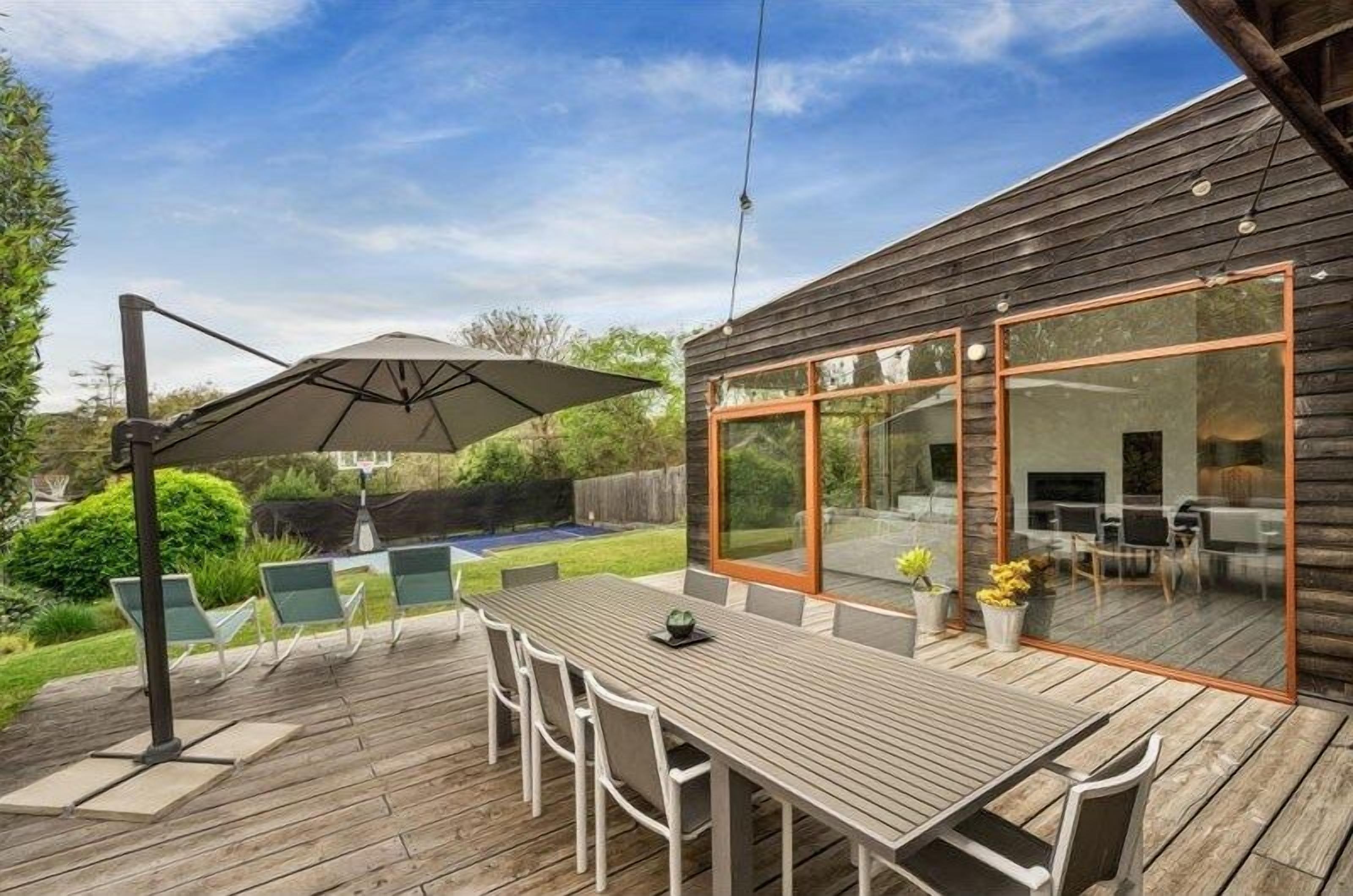Un patio exterior con una terraza de madera, una mesa de comedor con sillas y un paraguas grande.
