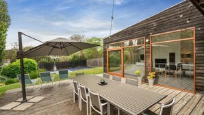 An outdoor patio with a wooden deck, a dining table with chairs, and a large umbrella. - Sorrento Sea Escape. (Sorrento)