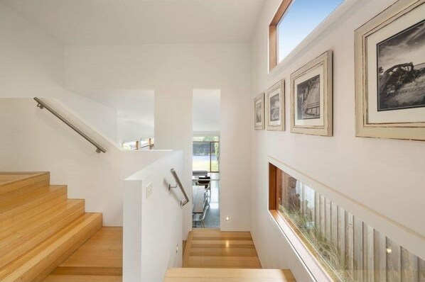 Un escalier avec des marches en bois et une rampe, menant à un espace intérieur dont les murs sont ornés de tableaux encadrés.
