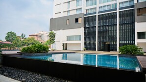 Ein modernes Gebäude mit Pool auf dem Dach, umgeben von Grünflächen und weiteren Gebäuden.