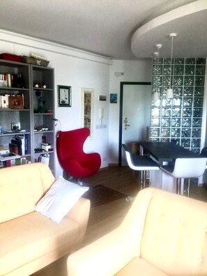 Una sala de estar moderna con una silla roja, un sofá color beige y una zona de comedor con una mesa y sillas.