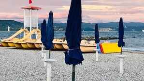 A beach with umbrellas and lounge chairs, a lifeguard tower, and a view of the sea and mountains. - Bellavista (Marina Julia)