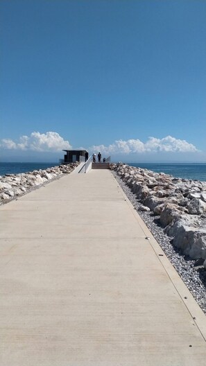 A concrete pathway leading to a building with a small shelter, surrounded by rocky terrain and the sea.