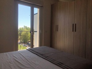 A bedroom with a bed, a wardrobe, and a balcony with a view of the outside.