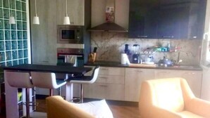 A modern kitchen with a curved island, bar stools, and a dining area with a sofa and chairs. - Bellavista (Marina Julia)