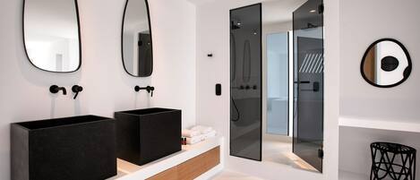 Un baño moderno con dos lavamanos negros, un espejo grande y una cabina de ducha de vidrio.