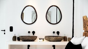 A modern bathroom with two oval mirrors, a stone sink, and a wooden headboard. - Psarou Black Villa II (Mykonos)
