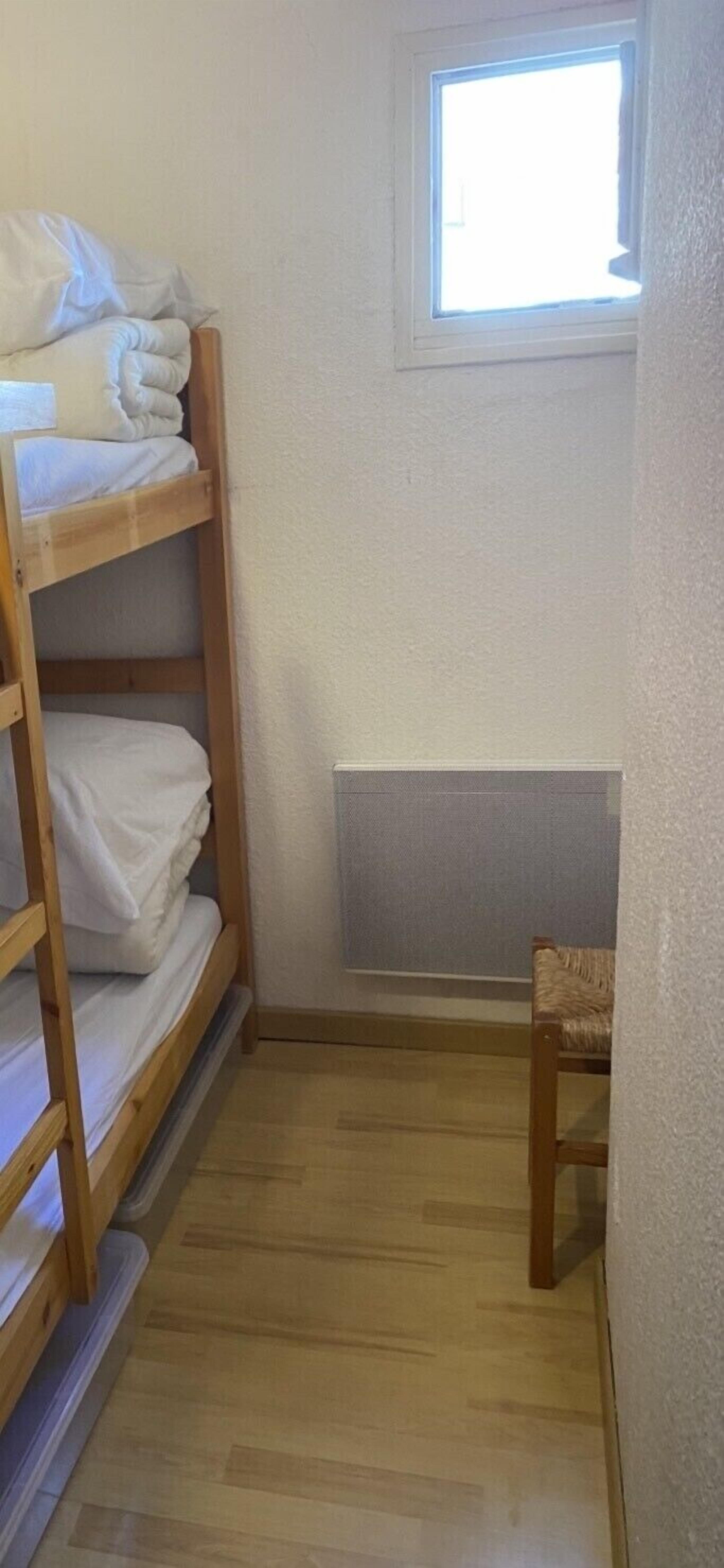 A small room with a bunk bed, a chair, and a window.