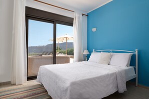 Ein Schlafzimmer mit einem großen Bett, weißer Bettwäsche, Blick durch eine Schiebetür, einem Korbstuhl und einer blauen Wand.