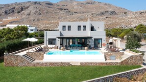 A modern two-story house with a swimming pool, stone walls, and a view of a mountainous landscape. - Villa Athena Lindos - 6 Bedroom Villa with Private Infinity Pool and Seaviews (Lindos)