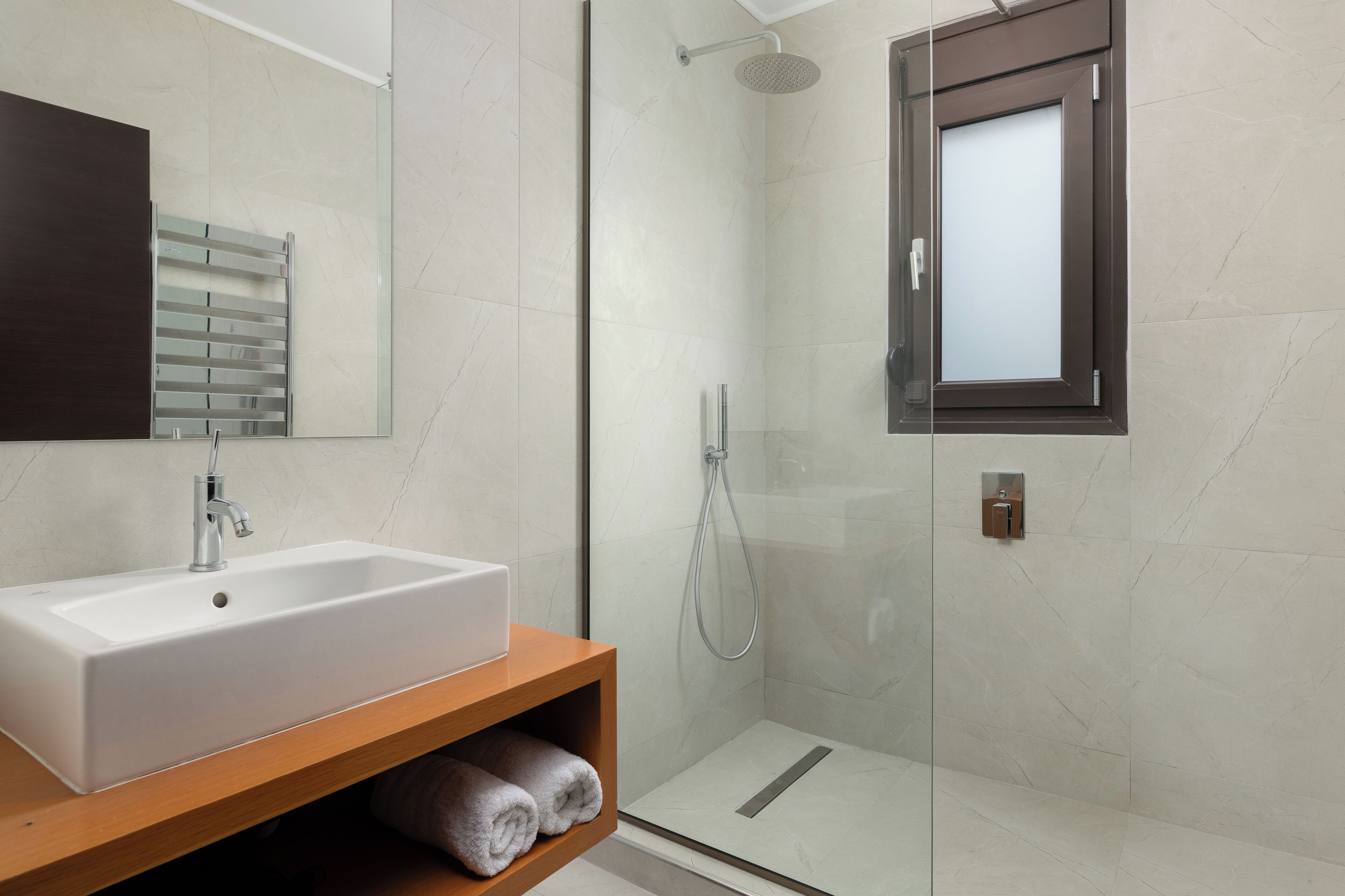 Een moderne badkamer met een wit wastafelmeubel, een douchecabine van glas en een houten wastafel.