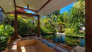 A serene indoor garden with a koi pond, stone seating, and lush greenery. - Tropical 6 Bedroom Villa Sanctuary (Hua Hin)