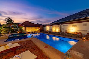 Piscina con un muro de piedra y una zona de estar techada.