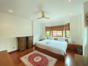 Un dormitorio con una cama grande, un ventilador de techo y una ventana con vistas a zonas verdes.