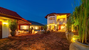 A courtyard with a brick pathway leading to a building with a red-tiled roof. There are large planters and outdoor furniture visible. - Tropical 6 Bedroom Villa Sanctuary (Hua Hin)