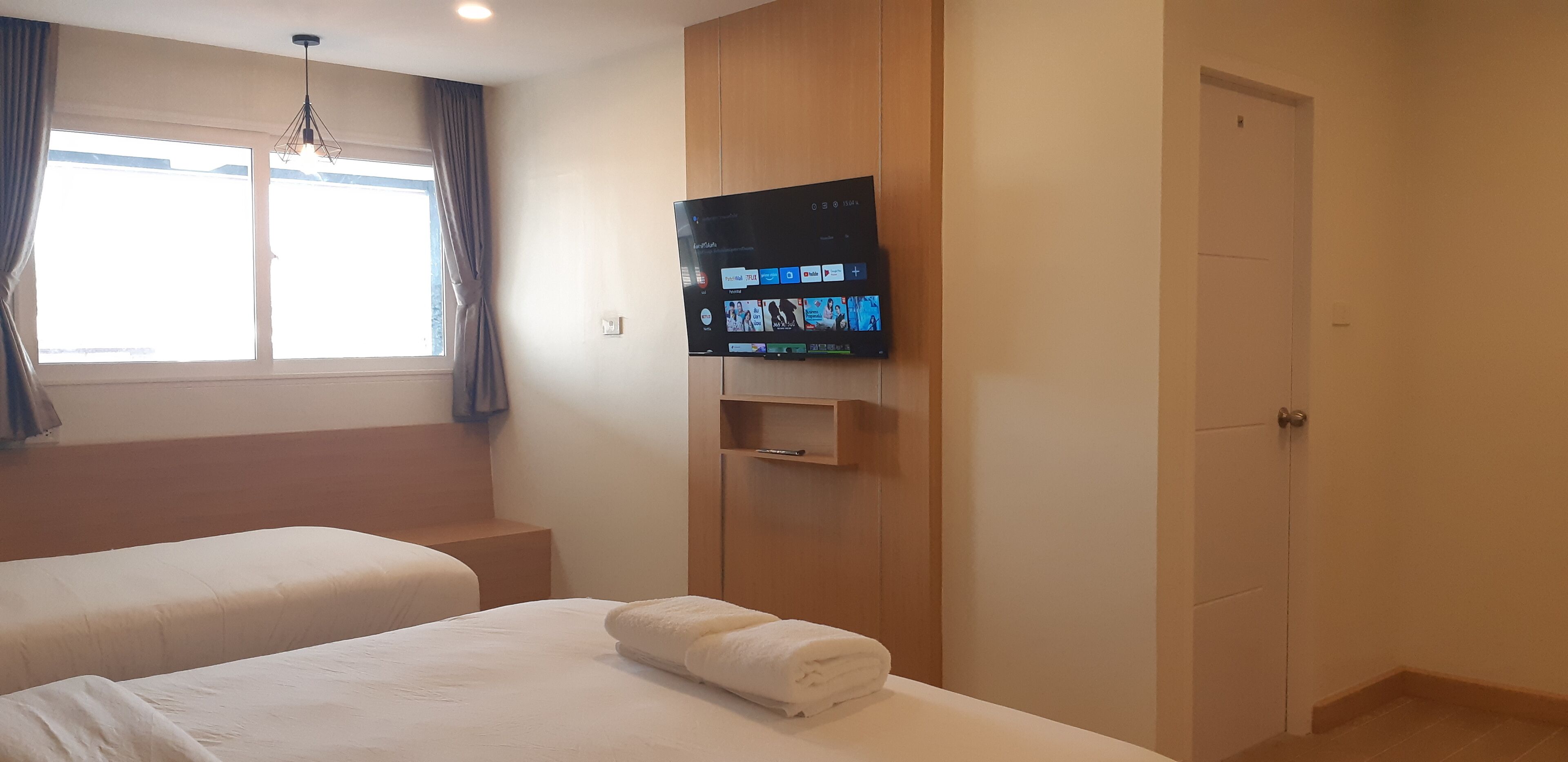 Hotellihuone, jossa on kaksi sänkyä, seinälle asennettu televisio, ikkuna, jossa on verhot, ja ovi.
