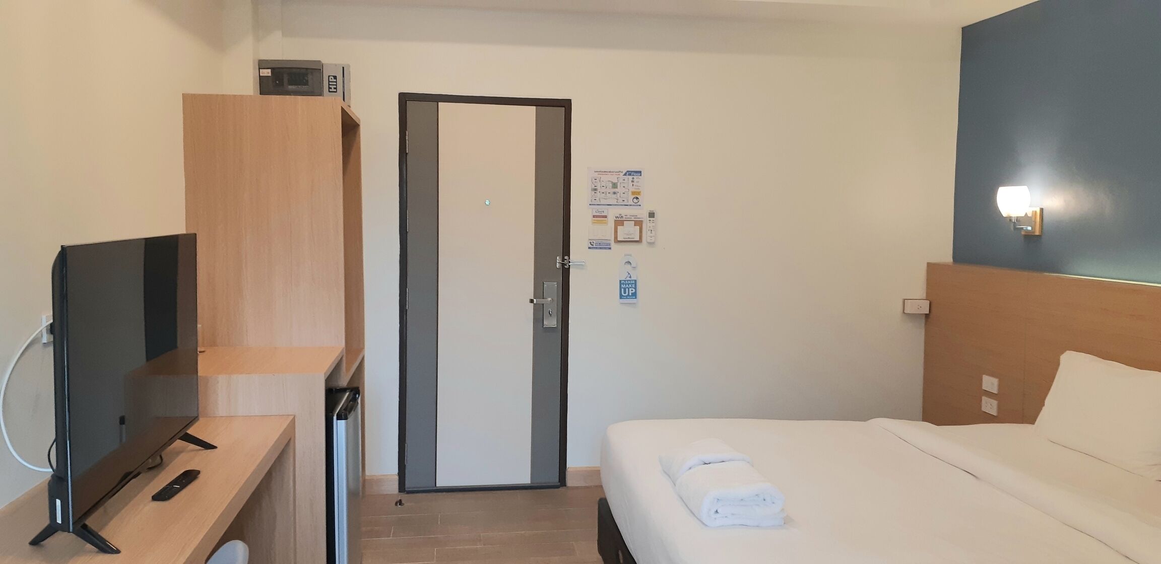 Habitación de hotel con cama, un televisor sobre un escritorio de madera, una puerta y una lámpara fijada a la pared.
