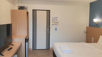 Habitación de hotel con cama, un televisor sobre un escritorio de madera, una puerta y una lámpara fijada a la pared.